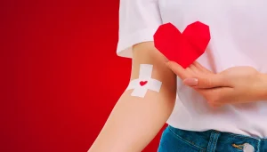 A person wearing a white shirt and blue jeans holds a red paper heard in their hand.